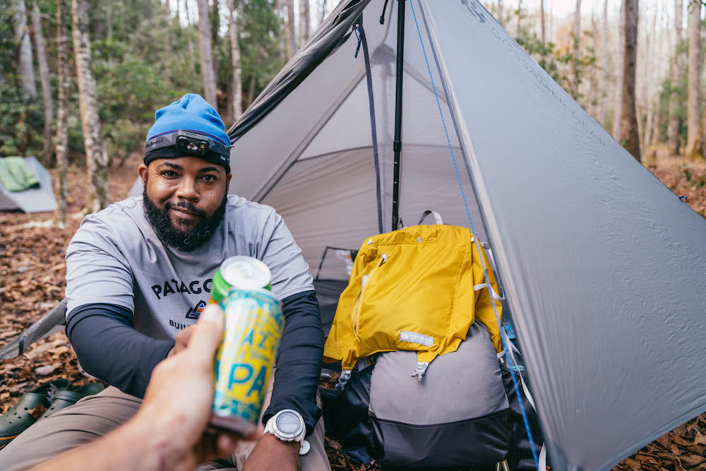A man camping and toasting with beers