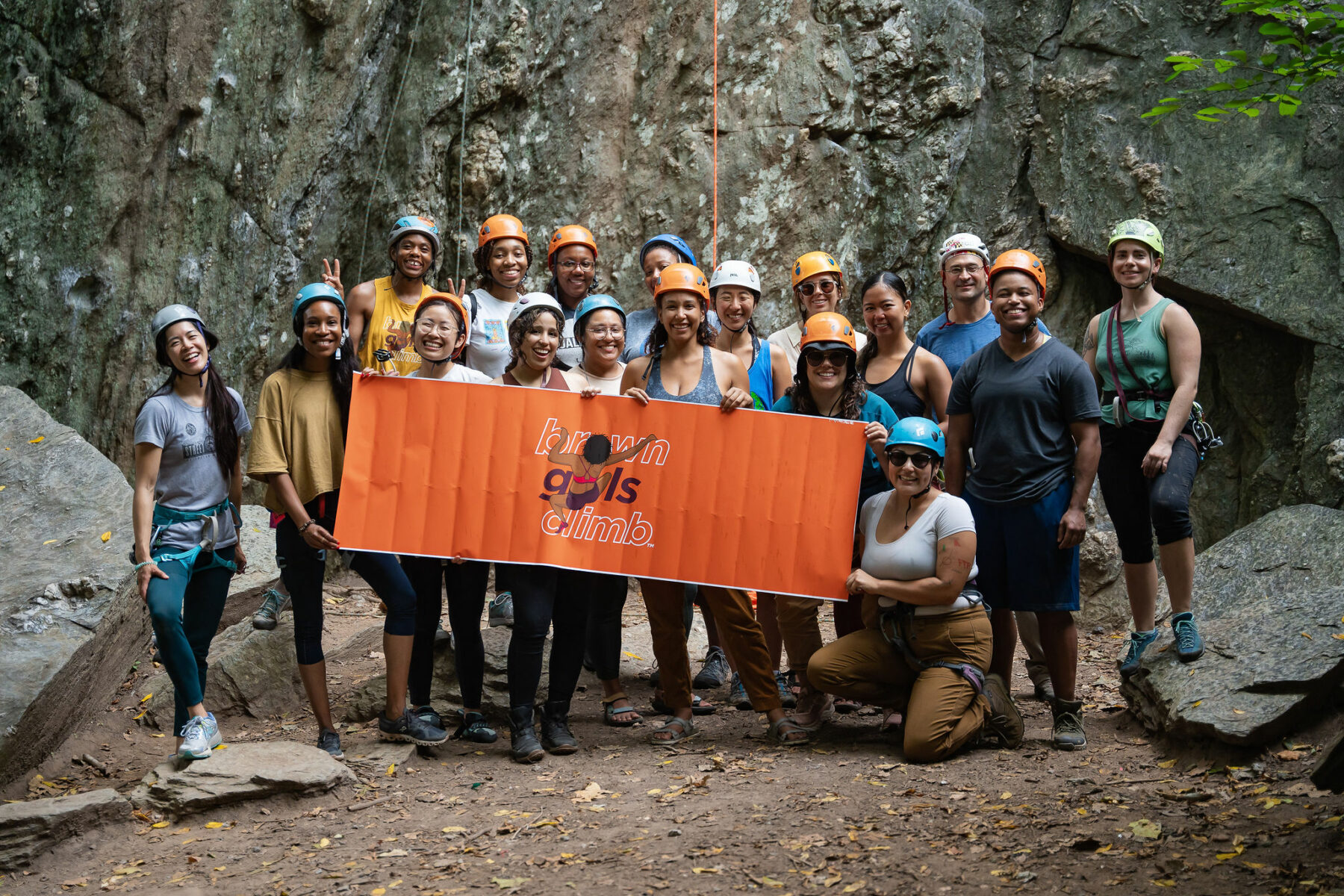 A group of climbers at a crag holding a sign that reads brown girls climb. 