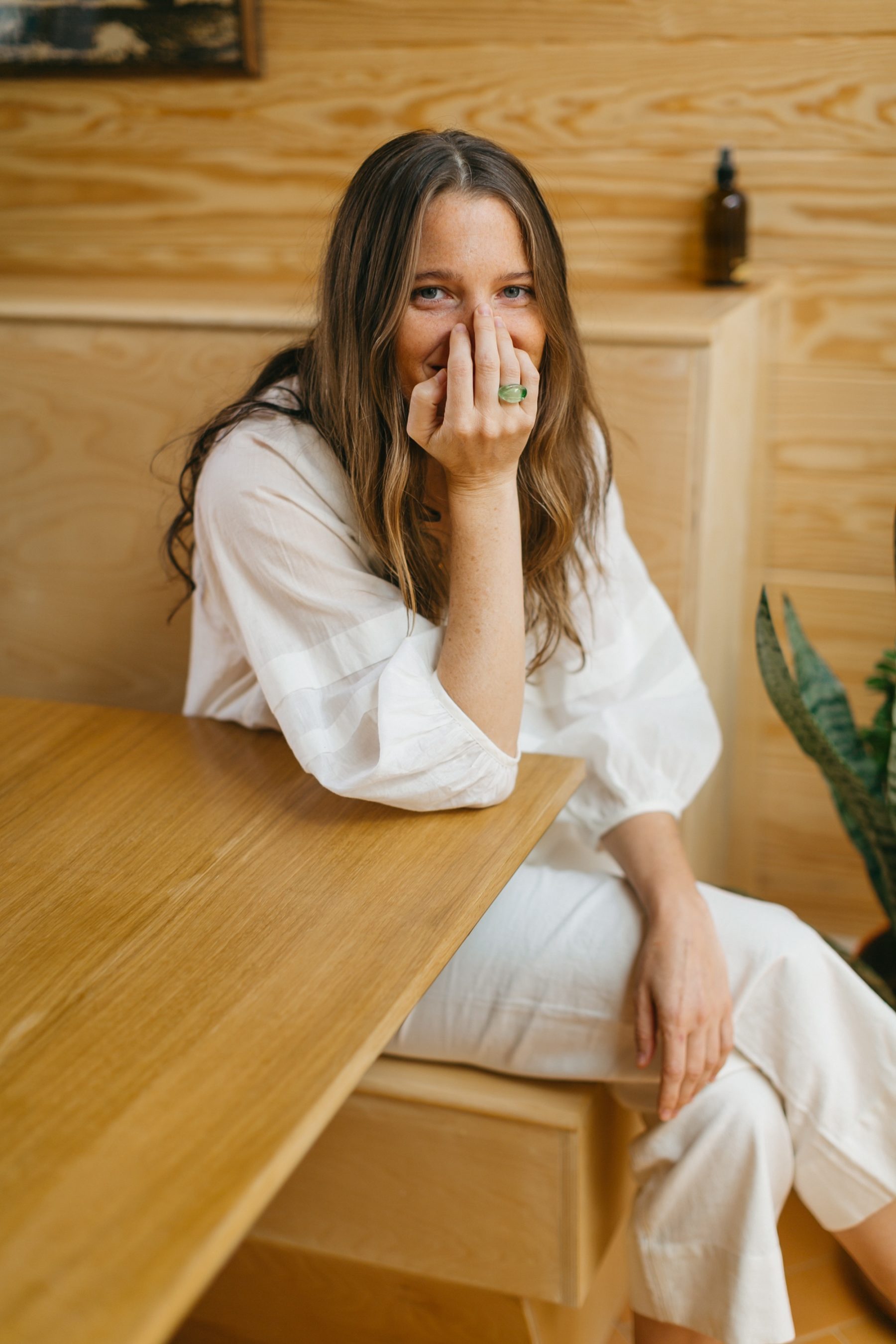 Woman sitting in a booth smiling with her hand over her mouth.