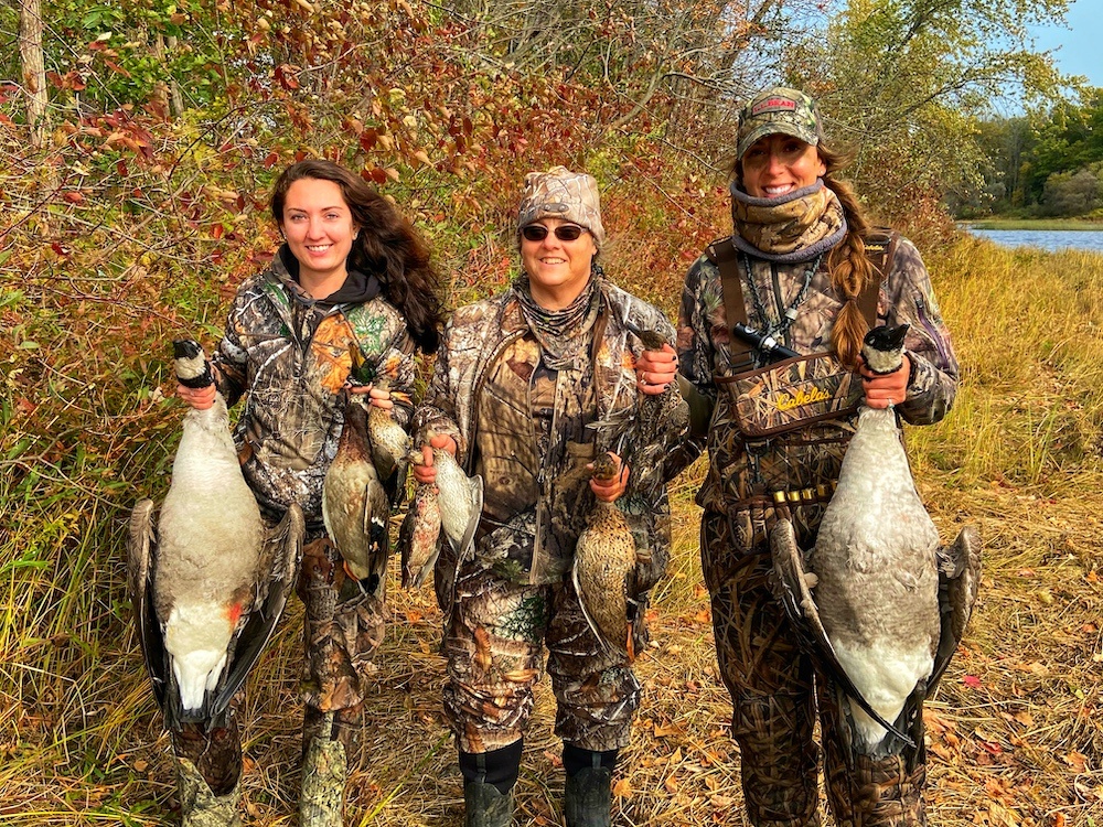 3 women in camp holding ducks and geese they have killed. 