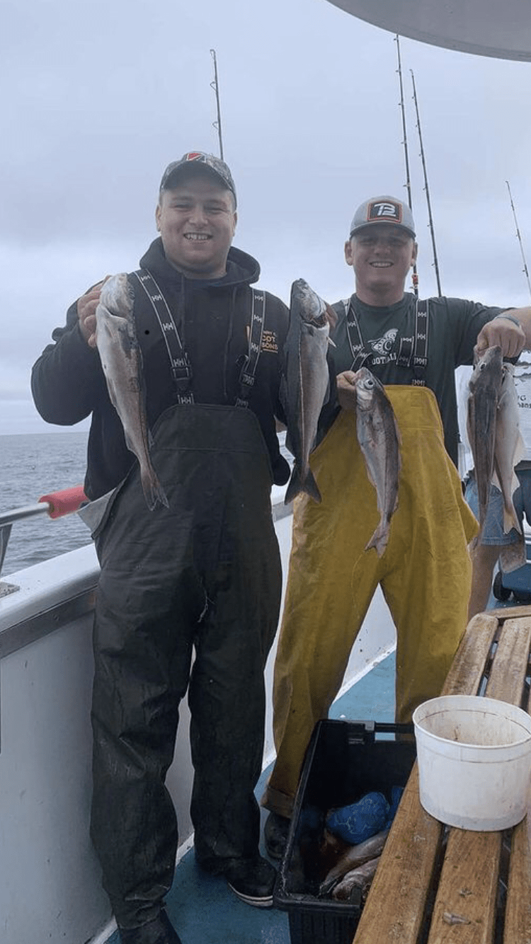 Two men on a boat in waterproof bibs holding fish at sea

