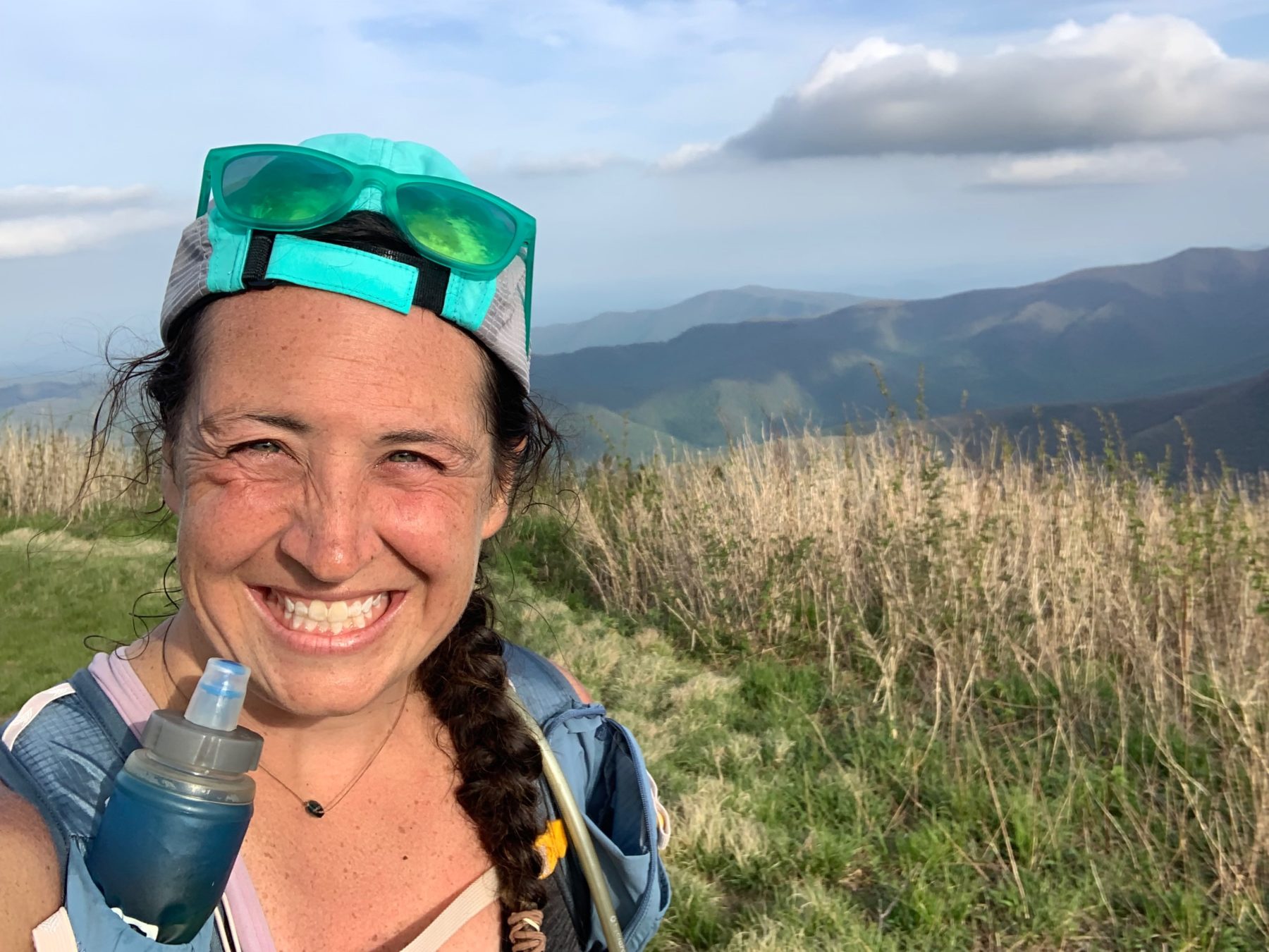A woman smiles from on top of a mountain mid-trail run.
