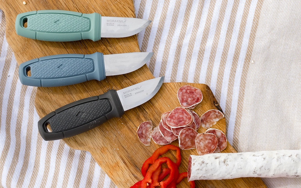 Three Eldris knives placed on a charcuterie board next to meat and veggies.