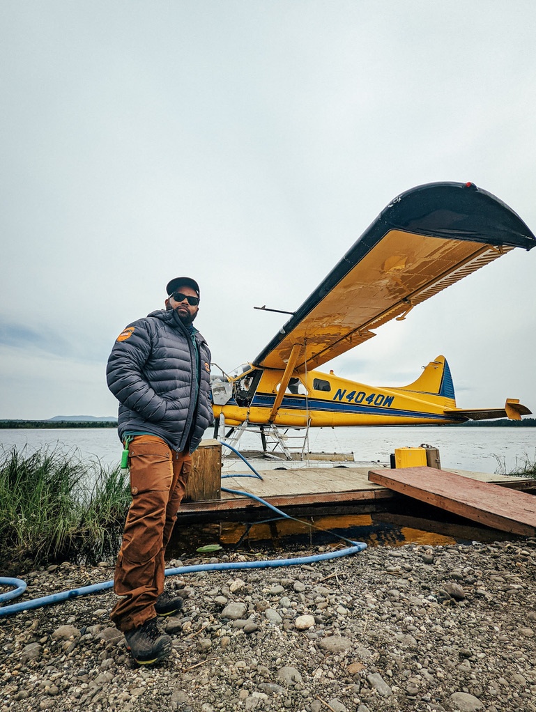 A man standing in front of a prop plane and lake