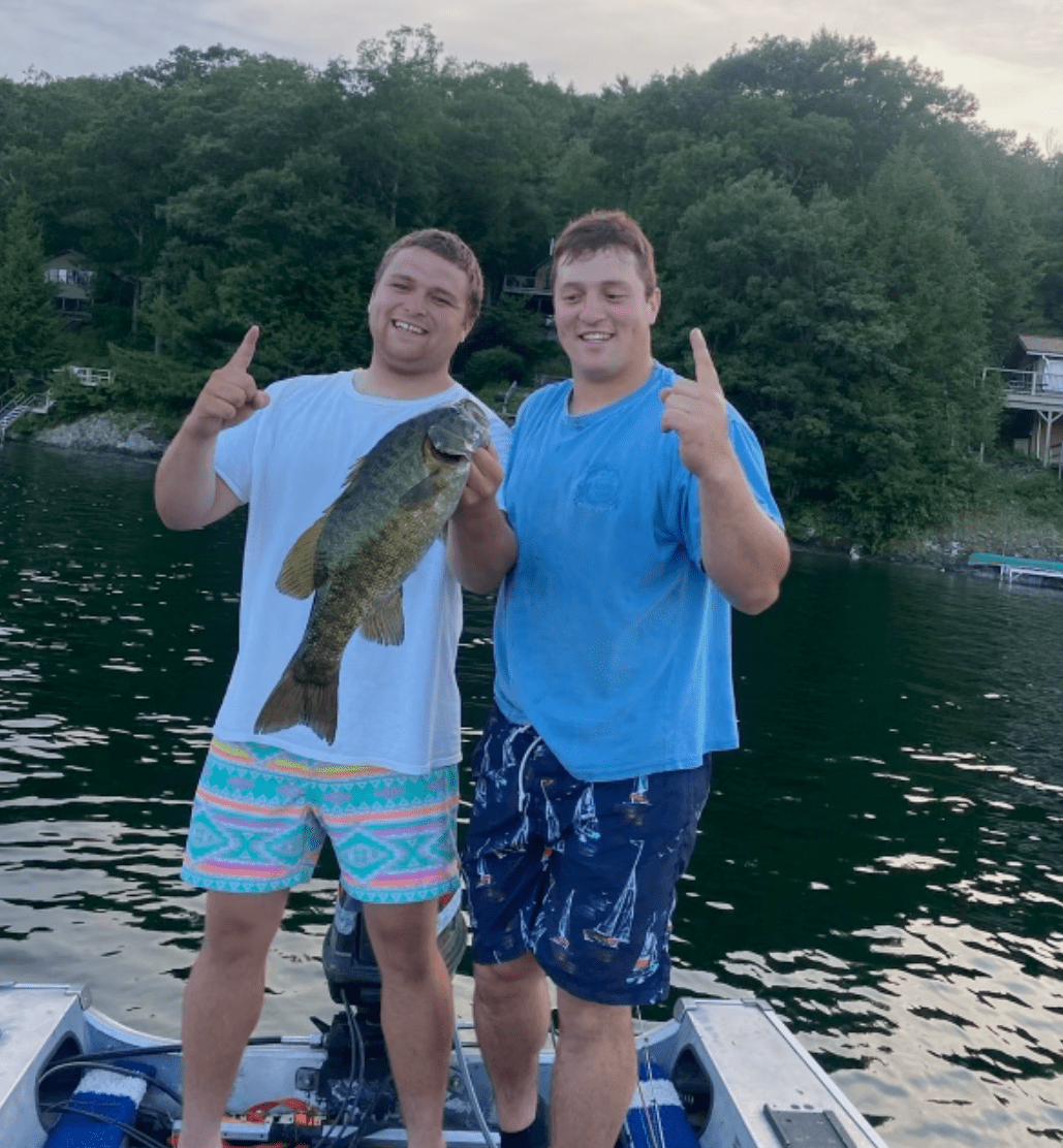 Two guys on a boat holding a fish and a number 1 finger in the air