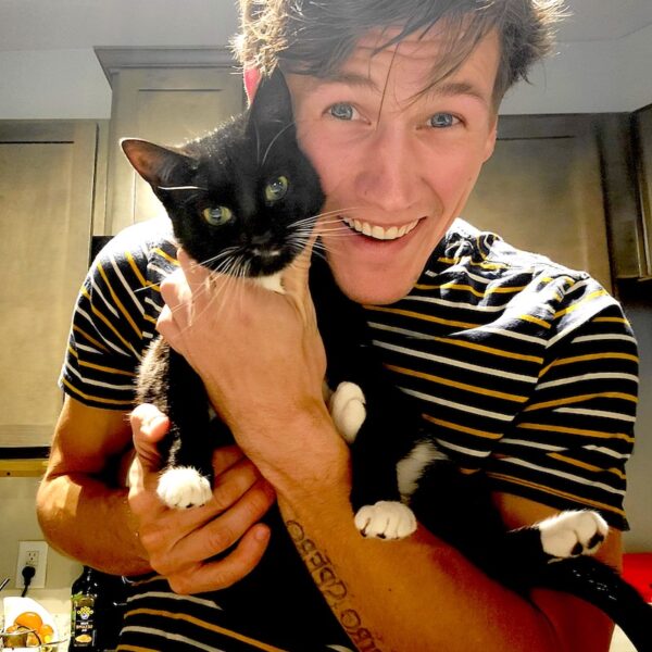 Tim Nooney in striped shirt holding his black and white cat