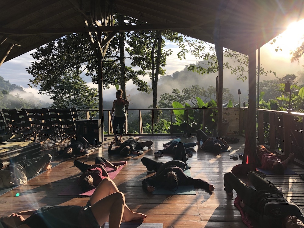 Women doing yoga with the jungle and a sunrise in the background